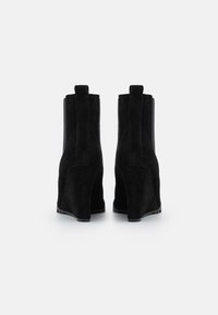 Černé semišové kotníkové boty s klínovým podpatkem. Obsahují texturované boky a zadní poutka. Hladká vnitřní podšívka a gumová podrážka.
