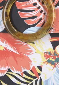 Blumenmusterstoff mit lebhaften roten, gelben und blauen Blumen auf schwarzem Hintergrund, versehen mit einem großen, durchsichtigen, bernsteinfarbenen kreisförmigen Ring.