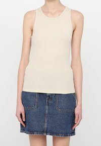 Ärmelloses Top aus leicht beigem Rippstoff mit Rundhalsausschnitt, kombiniert mit einem Jeansrock mit Fronttaschen und einem fransigen Saum.