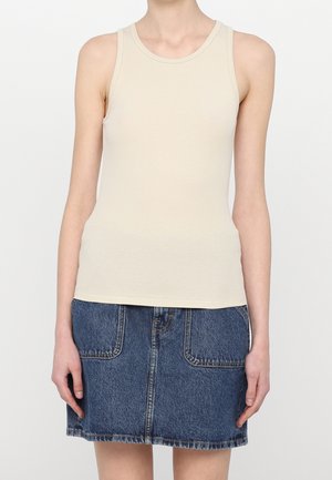 Débardeur en tissu côtelé beige clair avec un col rond, associé à une jupe en denim dotée de poches avant et d'un ourlet effiloché.