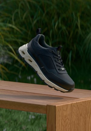 Tmavomodré športové topánky s hladkým koženým zvrškom, bielou medzipodrážkou a textúrovanými akcentami. Obsahujú šnúrky a pútko na päte.