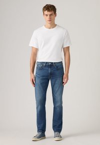 White cotton t-shirt, blue denim jeans, and grey sneakers. Jeans have a classic fit, with minimal detailing and no visible logos.