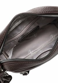 Interiér hnědé kožené tašky se zapínáním na zip, šedou podšívkou a jednou kapsou na zip. Textura je hrubá, bez viditelných vzorů.