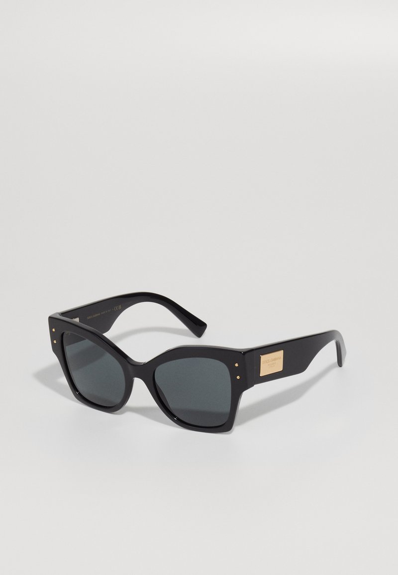 Ochelari de soare oversized negri cu lentile gri, având un cadru gros din plastic, accente metalice și un plăcuță cu logo pe partea exterioară.