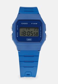 Montre numérique Casio F-91W avec un boîtier carré en plastique bleu, un bracelet en caoutchouc bleu et un affichage sombre affichant l'heure et des icônes de fonction.