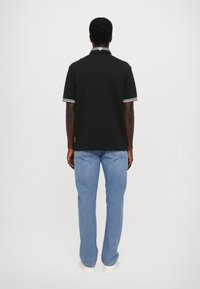 Svart polo-skjorte med hvitstripete krage og mansjetter, kombinert med lyseblå rette jeans. Enkel bakvinkel, minimal detaljer.