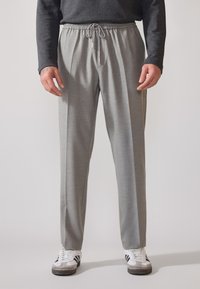 Graue Jogginghosen mit elastischem Bund und verstellbarem Kordelzug, aus strukturiertem Stoff und lockerer Passform, kombiniert mit weißen Sneakers.