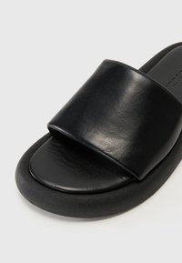 Sandale noire à glissière avec une large sangle en cuir lisse et une semelle en caoutchouc arrondie. Conçue pour le confort avec une esthétique minimaliste.