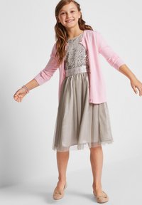 Un cardigan rose sur un haut en sequins argentés, associé à une jupe en satin gris clair. Des ballerines beiges complètent la tenue.