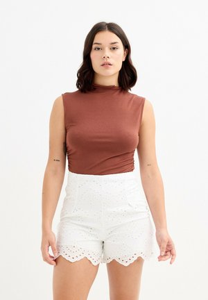 Top marrón sin mangas con cuello alto, combinado con shorts blancos de bordes festoneados que presentan patrones recortados y tela texturizada.