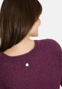 Lila gestrickter Pullover mit Rundhals, versehen mit einem silbernen Metalllogo-Knopf auf der Rückseite. Weicher Stoff und lässige Passform.