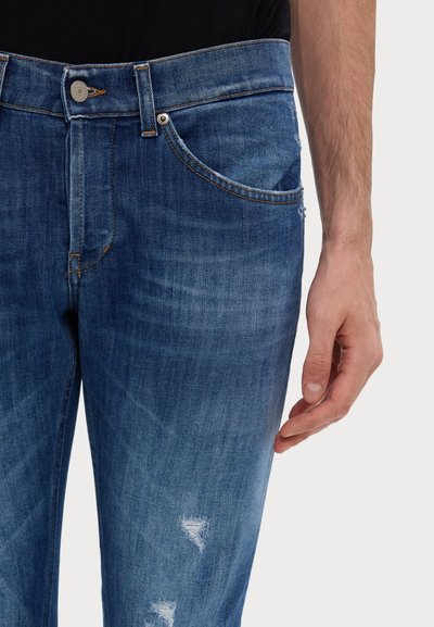 Siniset farkut slim fit -mallilla, joissa on hienovaraisia haalistumia, repeytymisiä ja kontrastivärisiä oransseja tikkejä, kiinnitetty metallinappilla.