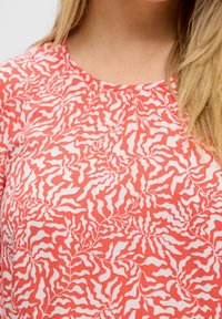 Blouse à motifs rouges et blancs avec un design abstrait ondulé, présentant un col rond et une texture de tissu douce et légère.