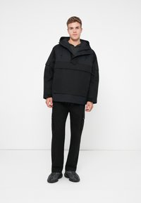 Casaco preto com capuz e um grande bolso frontal, com um corte descontraído e punhos elásticos, combinado com calças pretas justas e sapatilhas pretas texturizadas.