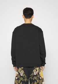 Svart crewneck sweatshirt med sänkta axlar, ribbade muddar och nederkant. Baksidan har en slät, enhetlig yta utan synlig branding.