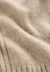 Tessuto a maglia beige con una fine trama, che mostra sottili variazioni di colore. Presenta dettagli a costine lungo i bordi. Morbido e flessibile.