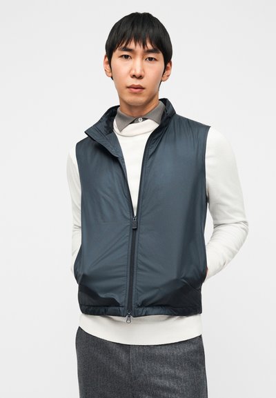 Μπλε σκουρόχρωμο αμάνικο γιλέκο με ψηλό γιακά, κατασκευασμένο από ελαφρύ υλικό, διαθέτοντας μπροστινό φερμουάρ και λεία, κομψή υφή.