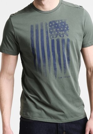 T-shirt en coton vert olive avec un graphique de drapeau bleu marine délavé avec des étoiles et des rayures ; comprend le texte "TOM TAILOR" en dessous de la conception.