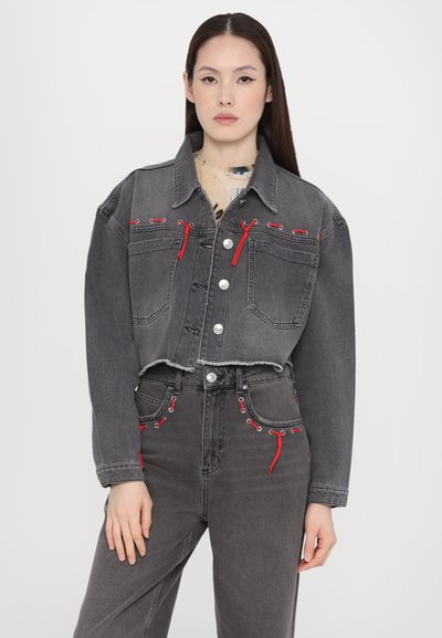 Grey cropped denim jacket with red accents, two front pockets, button closure, and a raw hem; paired with matching jeans featuring similar details.