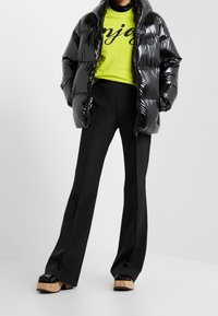 Chaqueta de plumas negra brillante con capucha, camiseta gráfica de color verde neón y pantalones de campana negros. Sandalias de cuña con suela de corcho acentuada.