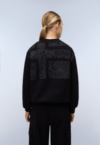 Černá mikina s texturovaným, vzorovaným zadním detailem v odstínech šedé. Disponuje kulatým výstřihem a žebrovanými manžetami.