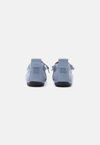 Hellblaue Lederschuhe mit abgerundetem Design, niedrigem Profil, Schnürsenkeln und kontrastierender schwarzer Außensohle. Logo sichtbar an der Ferse.