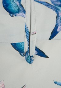 Světle šedá látka s potiskem modrých a růžových ptáků, s vázáním do smyčky blízko středu. Hladká textura, jemný lesk.