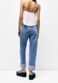 Top corto bianco testurizzato, jeans a vita alta blu chiaro con orlo risvoltato, e sandali con platform neri con cinturini blu.