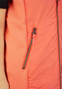 Padded Weste in Koralle mit einer seitlichen Reißverschlusstasche, ausgestattet mit glattem Stoff und kontrastierendem Design. Silberfarbene Reißverschlussbeschläge.