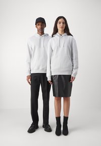 Due modelli stanno in piedi uno accanto all'altro. Entrambi indossano felpe grigio chiaro, il maschio con pantaloni e scarpe nere, la femmina con una gonna di pelle nera e stivaletti.