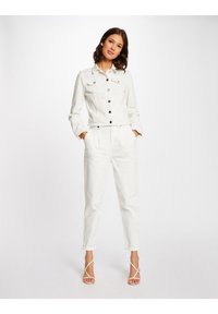 Giacca di jeans bianca con una vestibilità cropped, caratterizzata da bottoni neri e due tasche sul petto, abbinata a pantaloni bianchi a sigaretta e tacchi a strappo.