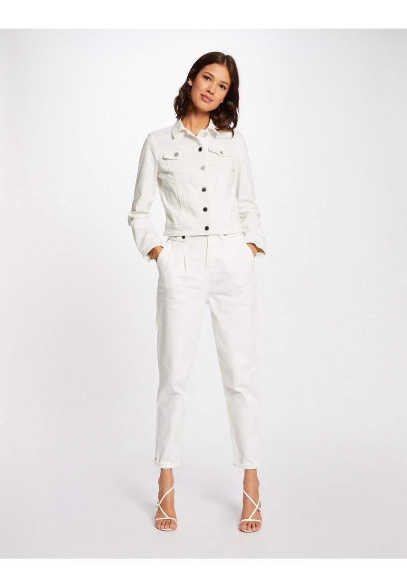 Giacca di jeans bianca con una vestibilità cropped, caratterizzata da bottoni neri e due tasche sul petto, abbinata a pantaloni bianchi a sigaretta e tacchi a strappo.