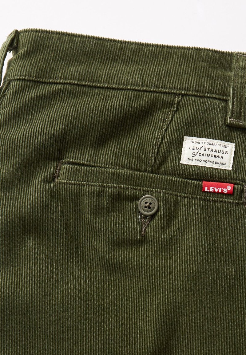 Zbliżenie na tylną kieszeń zielonych spodni z korduroy marki Levi's z zapięciem na guzik i dwoma oznaczeniami marki nad kieszenią.