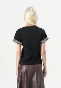 Black t-shirt with short sleeves featuring a decorative band of clear beads at the cuffs. Solid fabric, relaxed fit, simple neckline.