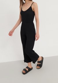 Bodysuit noir à rayures avec des bretelles fines, associé à un pantalon noir à jambes larges. Sandales noires chunky à double boucle et semelle texturée.