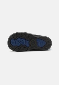 Semelle de chaussure en caoutchouc noir avec une texture antidérapante, accentuée de bleu et dotée de différents motifs de semelle pour une adhérence et une durabilité optimales.