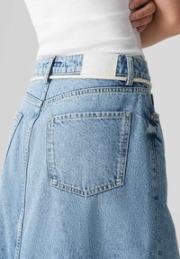 Gonna di jeans azzurra chiara con vita alta, tasche posteriori e etichetta bianca in vita. Tessuto testurizzato con dettagli di cucitura.