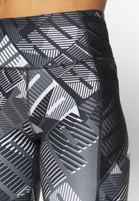 Vysoké sportovní legíny s geometrickým černobílým vzorem. Vyrobeny z elastické tkaniny s kontrastní texturou a švy.