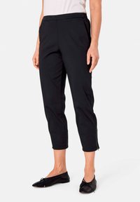 Zwarte cropped broek gemaakt van een soepele stof, met een rekbare tailleband en zijritsen aan de onderkant voor gemakkelijk aan- en uittrekken.