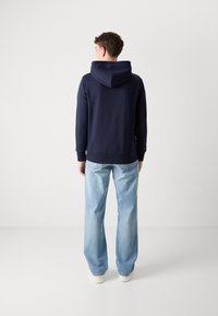 Hoodie en coton bleu marine avec capuche à cordon, poignets et ourlet côtelés. Associé à un jean en denim bleu clair à coupe ample.