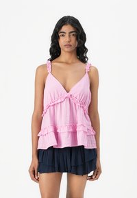 Rosa Baumwolltop mit Rüscheträgern und Saum, V-Ausschnitt und geschichteter Optik, kombiniert mit einem marineblauen gefalteten Rock.