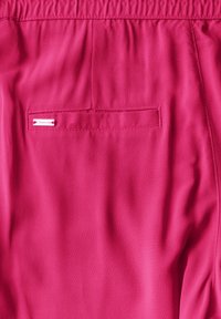 Klart rosa shorts med elastisk midjeband, som har ett litet bakficka och en märkeslapp, tillverkade av slätt och lätt tyg.