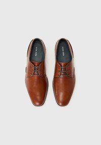 Brown leather shoes with a rounded toe, smooth texture, lacing detail, and black insoles marked "PIER ONE." Sole is flat and dark.