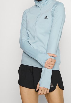 Pullover azzurro chiaro con zip a quarto realizzato in tessuto morbido, con maniche lunghe e aperture per il pollice, con un piccolo logo Adidas nero sul petto.