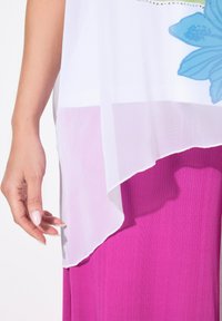 Hvid, gennemsigtig bluse med blomsterdesign og sølvdetaljer lag på en tekstureret, lys pink plisseret nederdel, der viser lagdelte stofdetaljer.