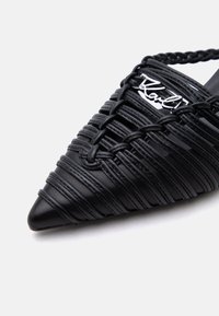 Μύτος mule σε μαύρο με μυτερή μύτη, πλεκτές δερμάτινες λουρίδες και ασημένια λεπτομέρεια με το λογότυπο "Karl" στο επάνω μέρος.