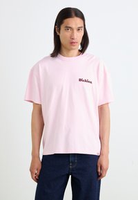 Light pink oversized t-shirt, cotton fabric, round neck, featuring dark brown embroidered "Dickies" logo on the left chest area.