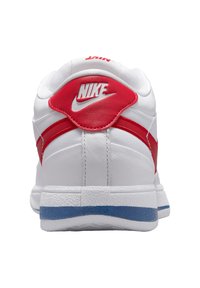 Weißer Nike-Sneaker mit roten Akzenten, gepolstertem Kragen und strukturierter Sohle. Verfügt über ein markantes rotes Swoosh-Logo und einen kontrastierenden blauen Streifen.