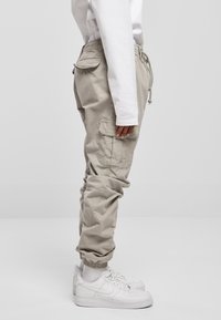 Beige Cargo-Hosen mit einem elastischen Bund, Seitentaschen und Bündchen. Kombiniert mit weißen Sneakers, die eine glatte Textur und einen lässigen Sitz zeigen.