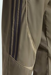 Khaki športové nohavice s tromi námorníckymi pruhmi po boku, s hladkým povrchom a jemným kontrastným stehom pozdĺž švov.